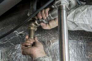 Close-up of a plumber's hands installing steel pipes indoors, showcasing skilled manual work.